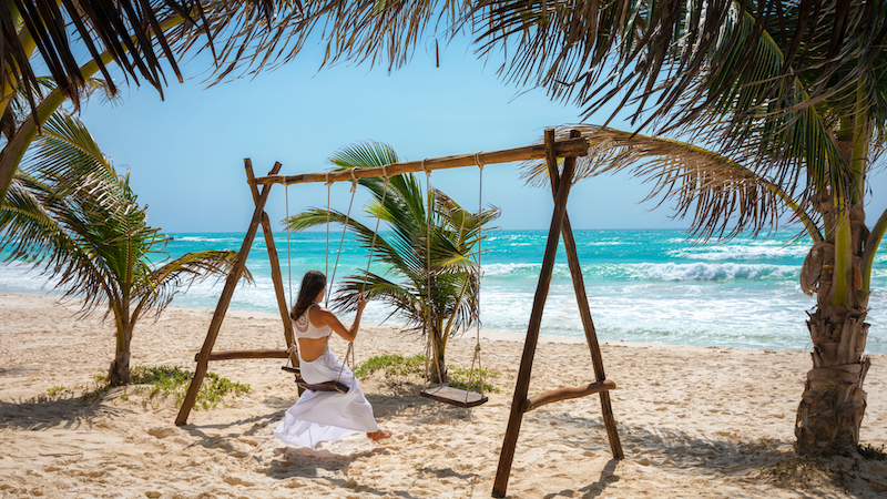 Image of a woman swinging on a beach in Tulum